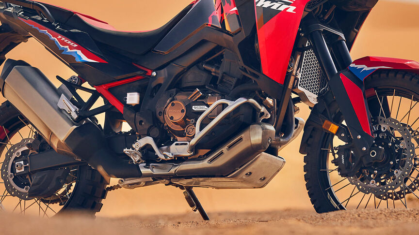 Model riding CRF1100L Africa Twin motorbike in a desert location.