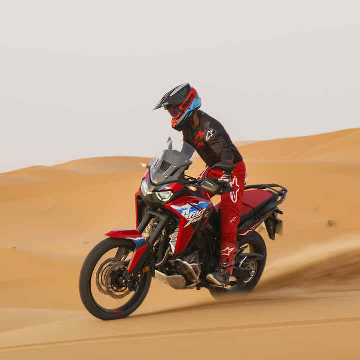 Model driving CRF1100L Africa Twin bike on a road in a desert location.