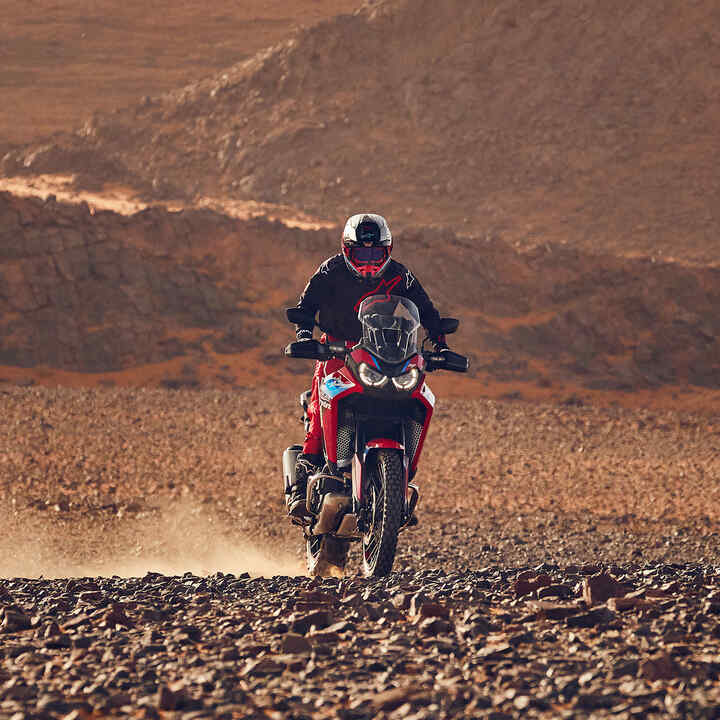 Model driving a CRF1100L Africa twin motorbike in a desert location.