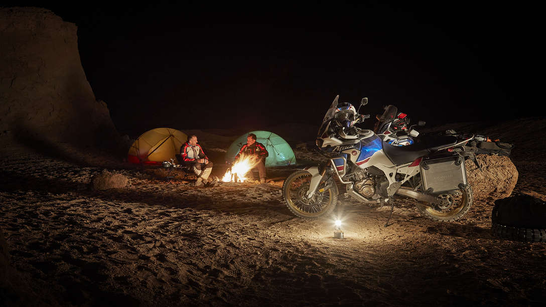 Two people camping and Honda Africa Twin Adventure Sports side view parked at night.