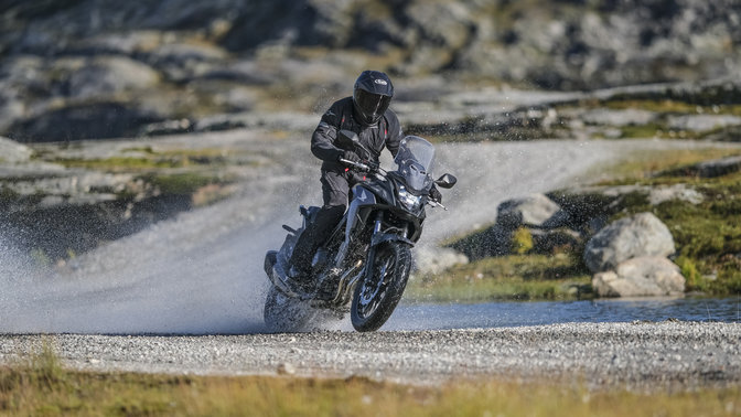 front angled view of rider riding a honda cb500x adventure motorcycle on a gravel road