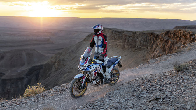 side angled view of a rider standing up on a africa twin adventure sports motorcycle on a dirt track