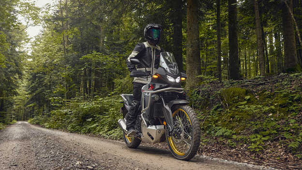 Model riding a Honda XL750 Transalp in forest location.