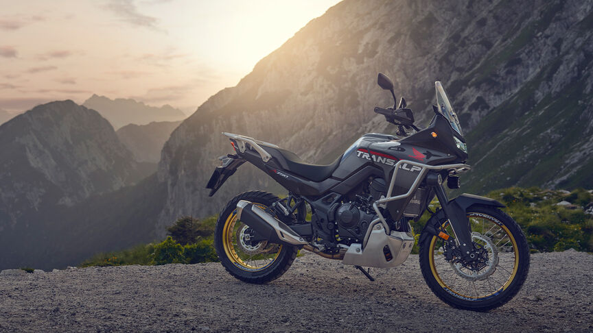 Model riding XL750 Transalp motorcycle in a forest location.
