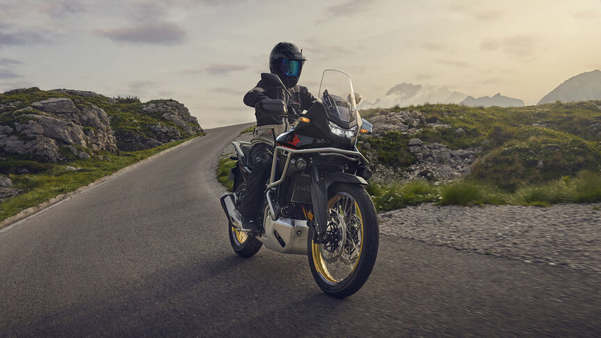 Model riding XL750 Transalp motorcycle in a forest location.