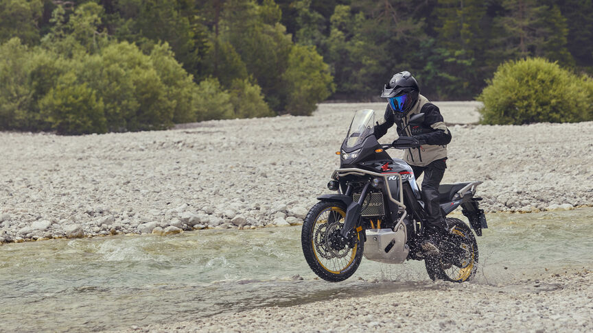 Model riding XL750 Transalp motorcycle in a forest location.