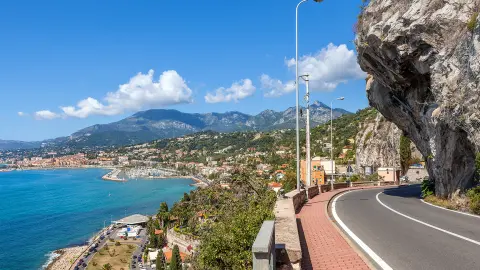 Scenic road under blue sky along Mediterranean sea coastline on French-Italian border.