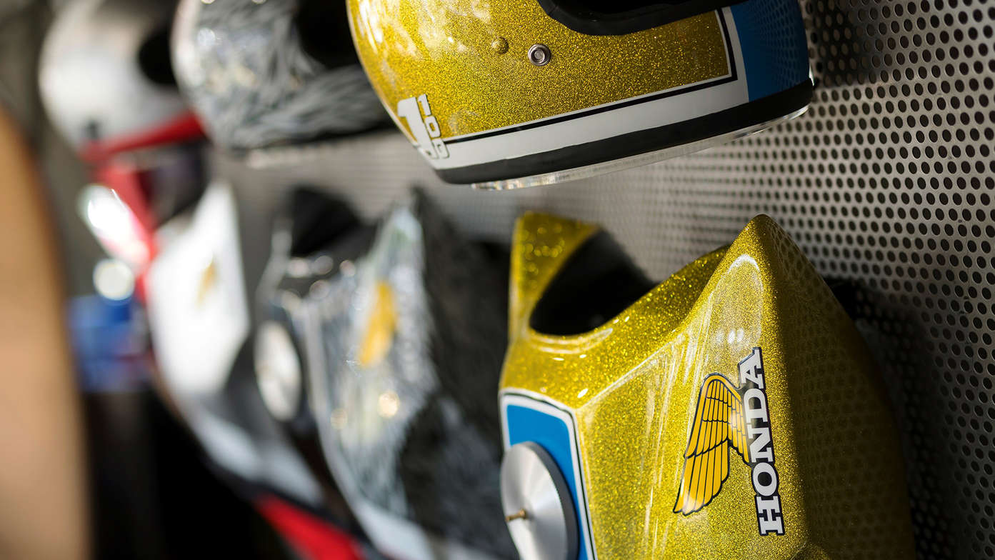 Customized helmets and fuel tanks hanging on a wall.