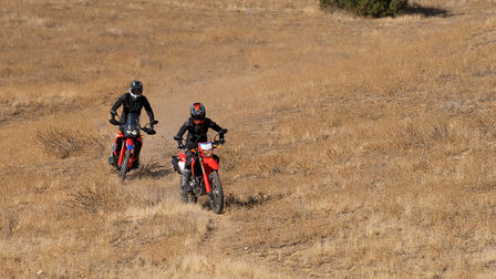 Honda off-road motorcycle, front three-quarter view, riding on dirt road location.