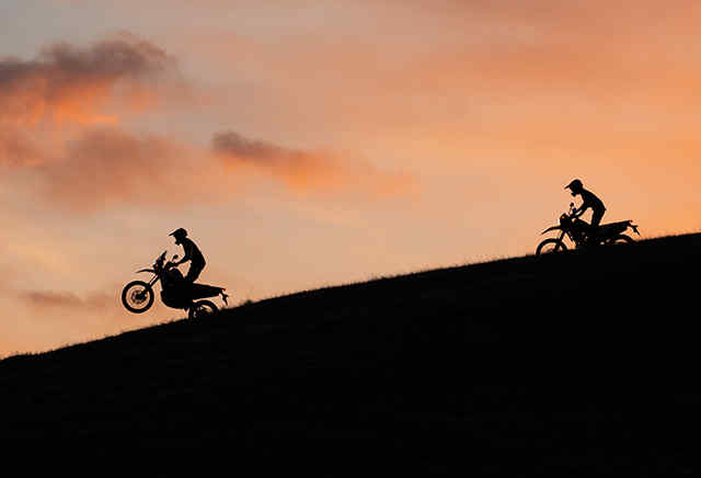 Two 300 series Honda motorbikes riding down a hill in the sunset