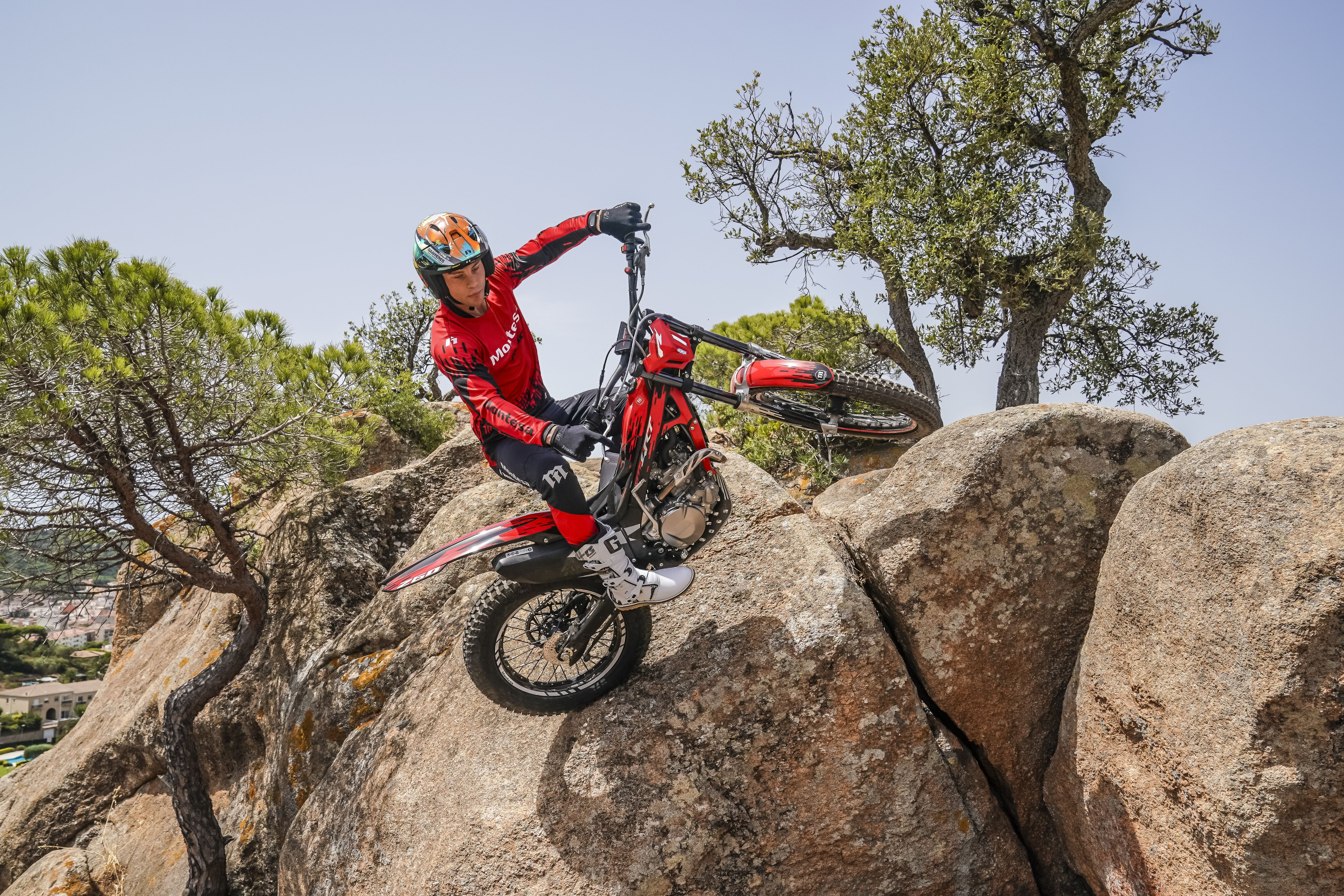 Rider maneuvering a red Montesa Cota 4RT 260R motorcycle up steep boulders on a sunny day.