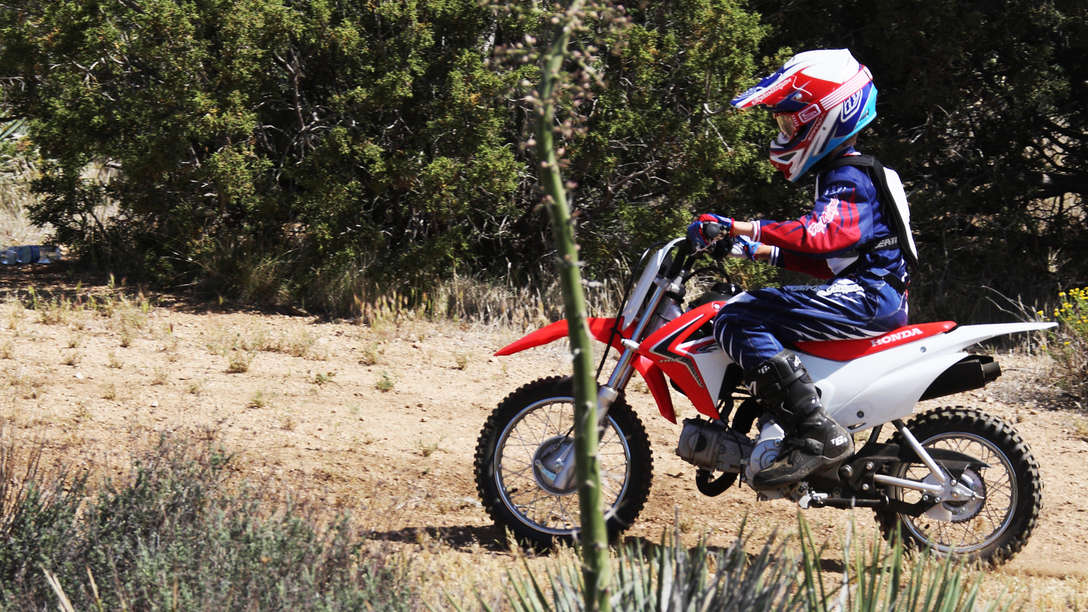 Side on, threequarter view of CRF110F with rider in dirt race location. Left facing.