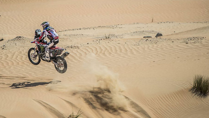 Rear three-quarter facing Honda CRF450 riding through sand dunes.