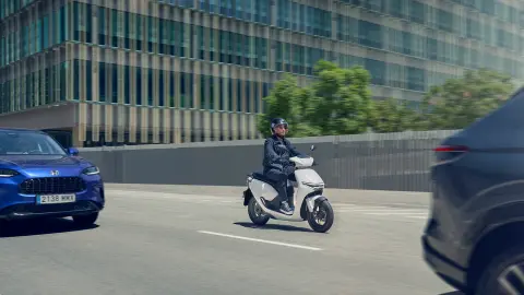 Rider driving a Honda CUV e motorcycle in a city location.