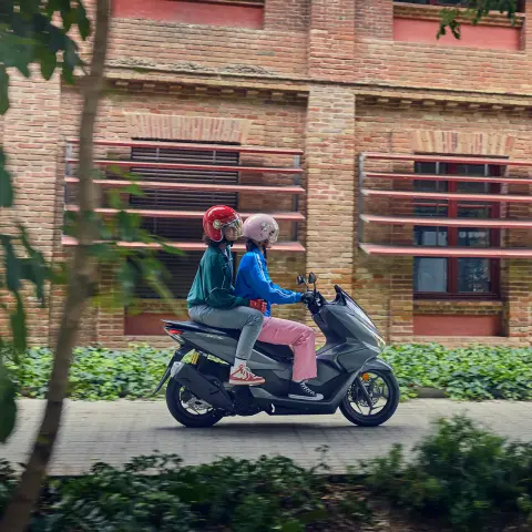 Side shot of models riding the PCX125 motorcycle in a city location.