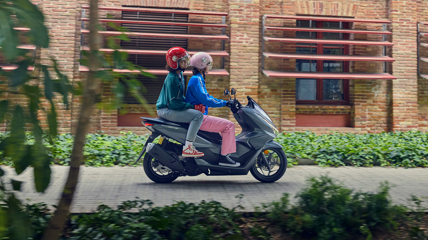 Side shot of models riding the PCX125 motorcycle in a city location.