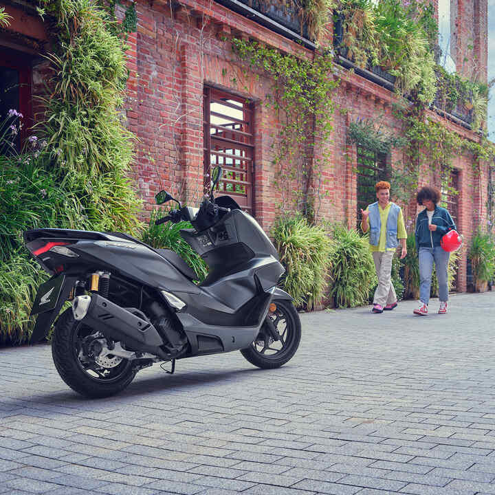 Models walking towards the PCX125 motorcycle.