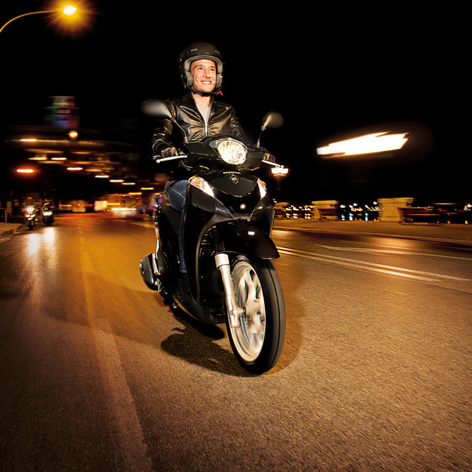 Black Honda SH Mode scooter front-threequarter view with rider. Right-facing (Road location).