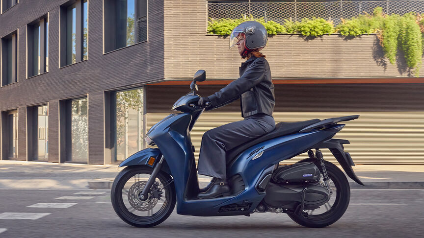Lady riding a side facing Honda SH350i in city location.