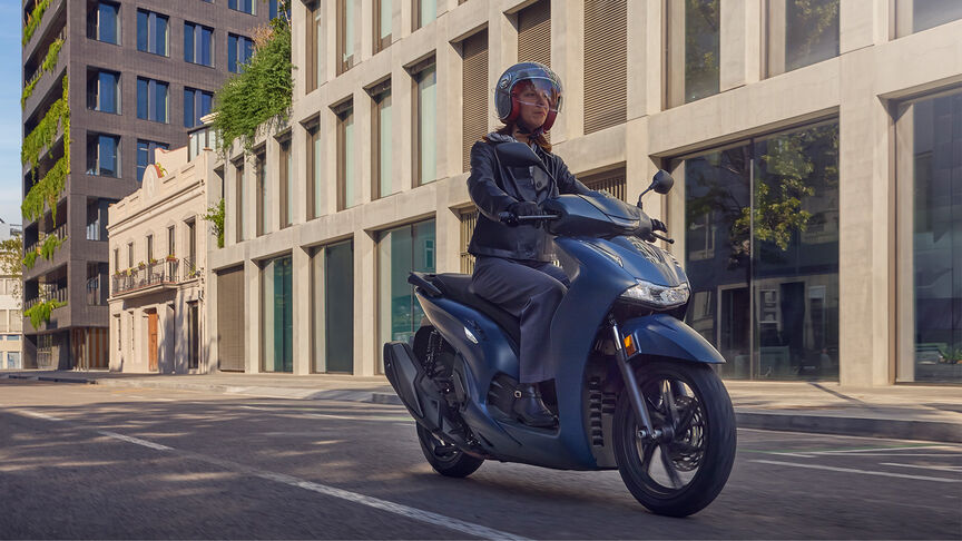 Lady riding a side facing Honda SH350i in city location.