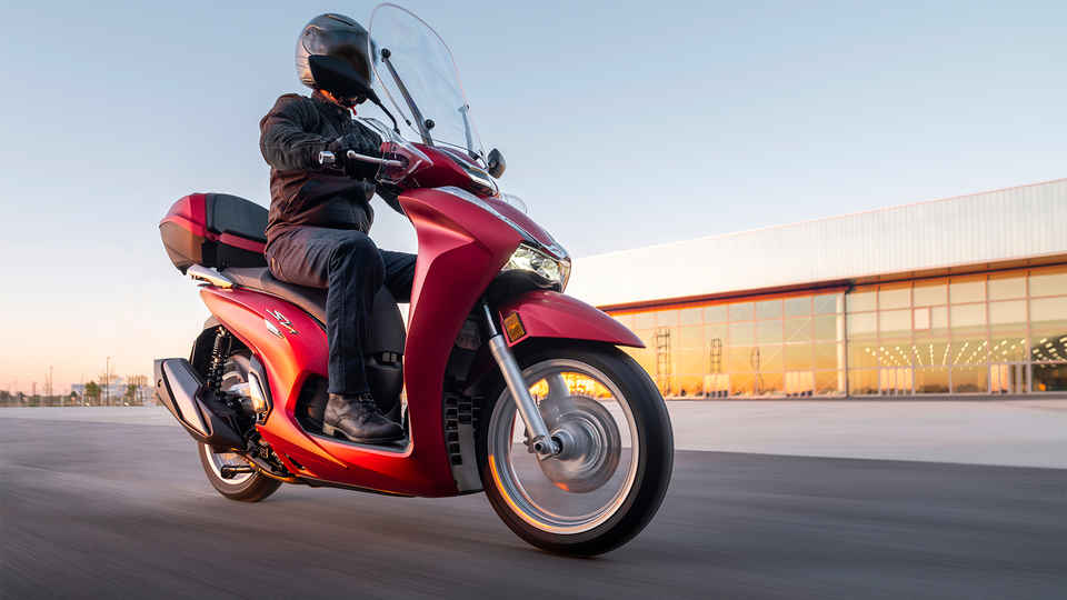 Honda SH350i, 3-quarter front right, with rider, on the road, red bike