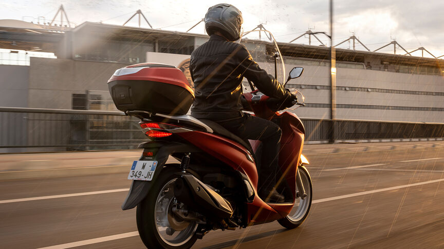 Honda SH350i, 3-quarter front right, with rider, on the road, red bike