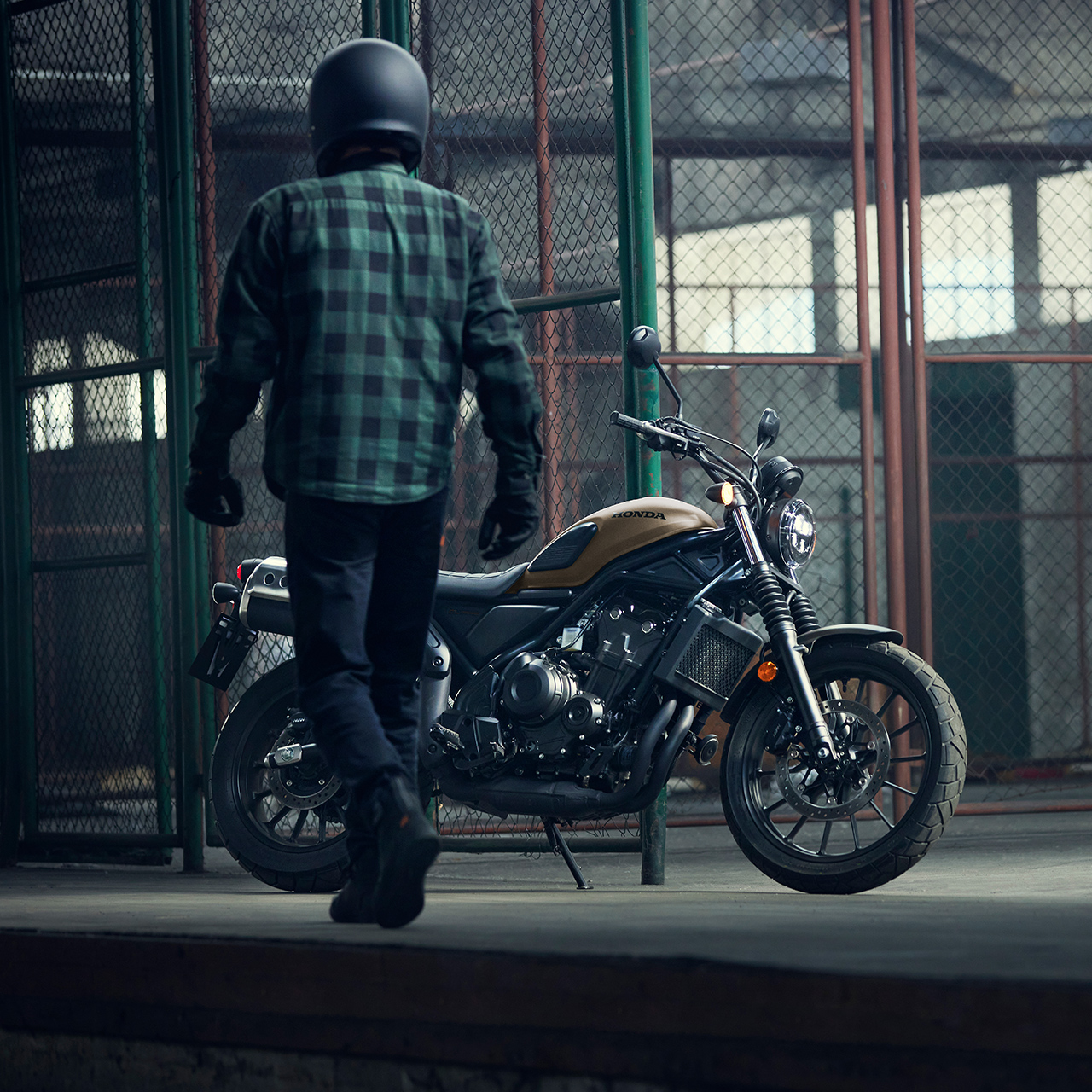 Rider walking alongside a parked Honda CL500 motorcycle in a warehouse location.