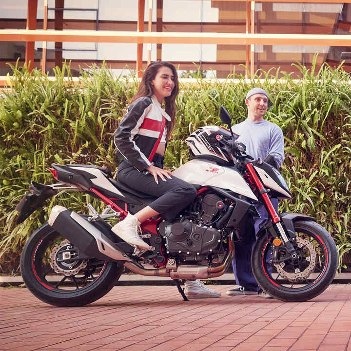 Female rider on Honda CB750 Hornet with man dancing.