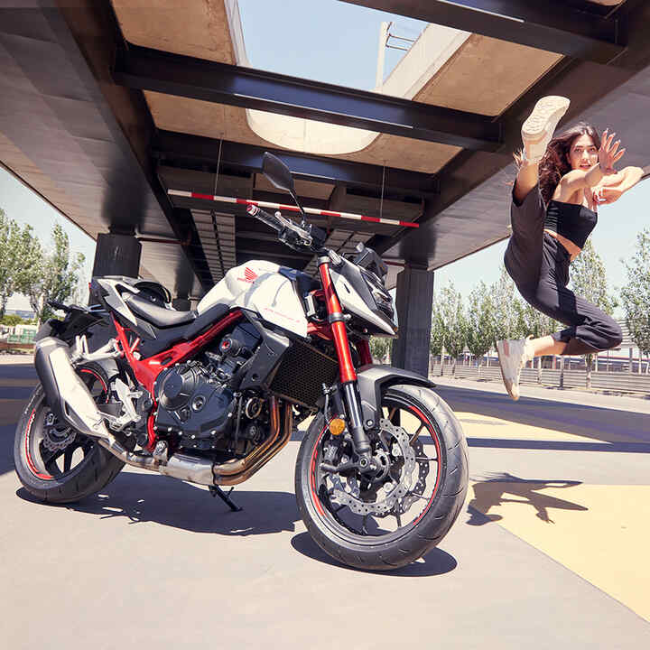 Female dancer jumping in air next to Honda CB750 Hornet.