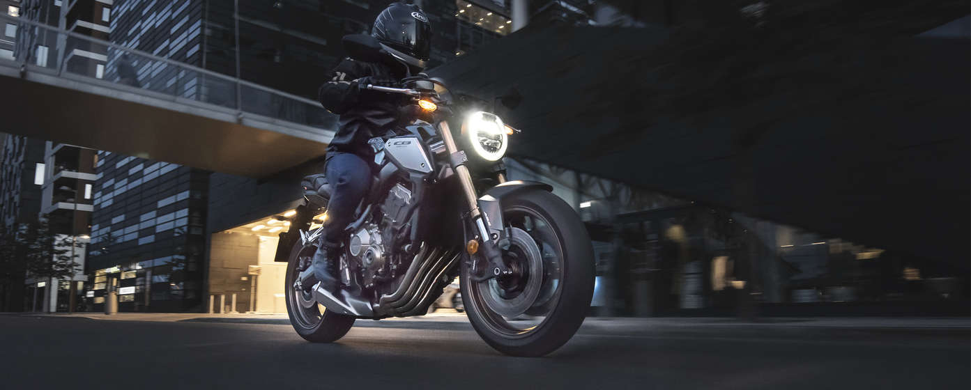 side angled view of rider on a cb1100 rs street motorcycle riding through a city at night