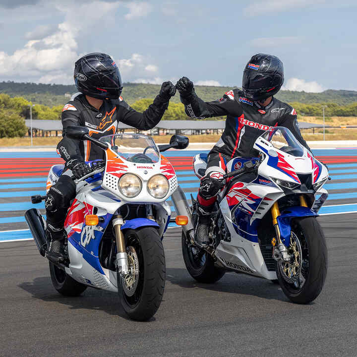 Two riders sitting on front facing Honda Fireblades bumping fists on the race track.