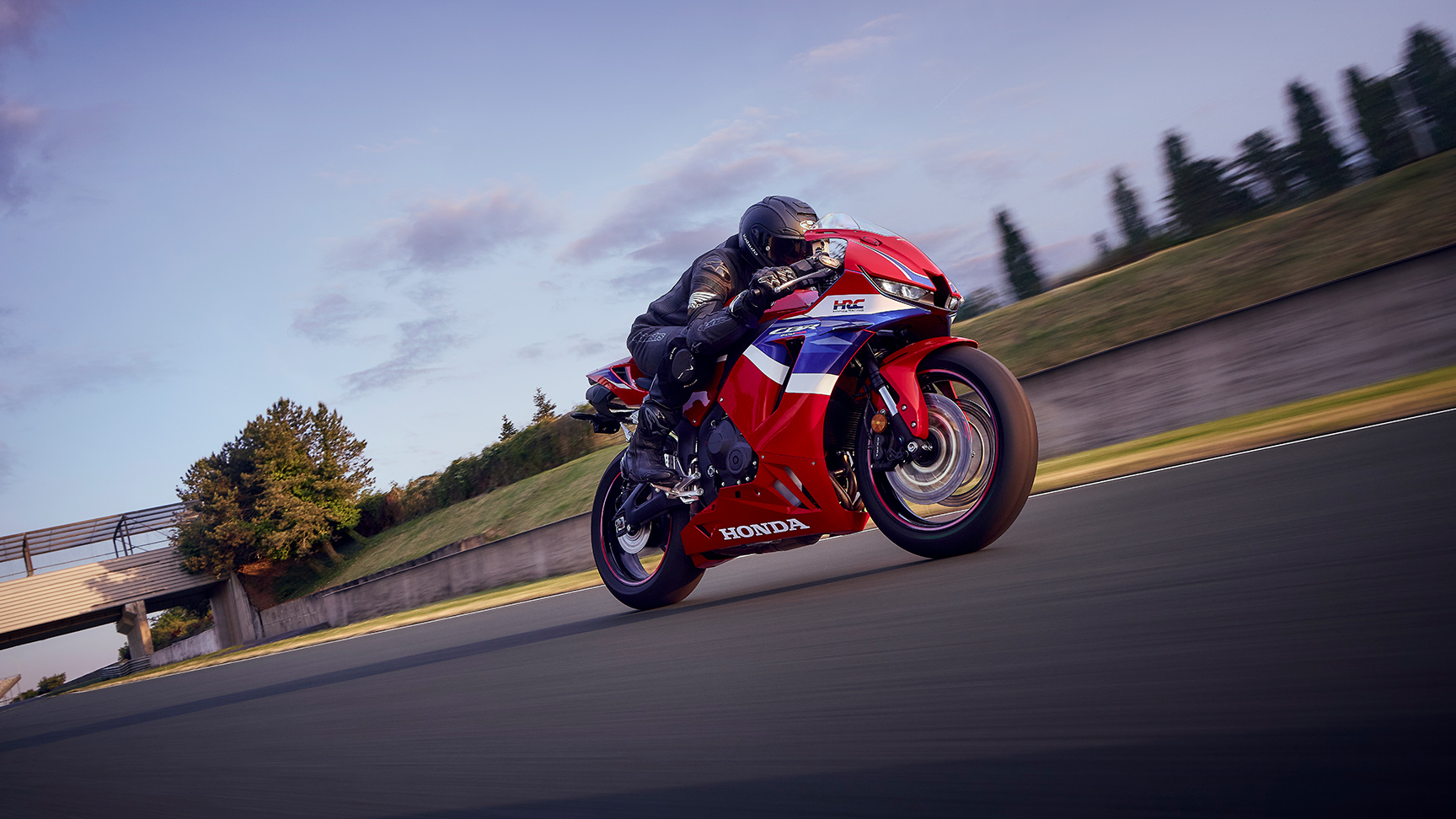 CBR600RR on track with rider in corner at sunset.