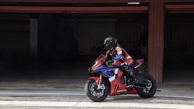 side angled view of rider leaving garage riding a red honda cbr1000rr-r fireblade sp super sport motorbike