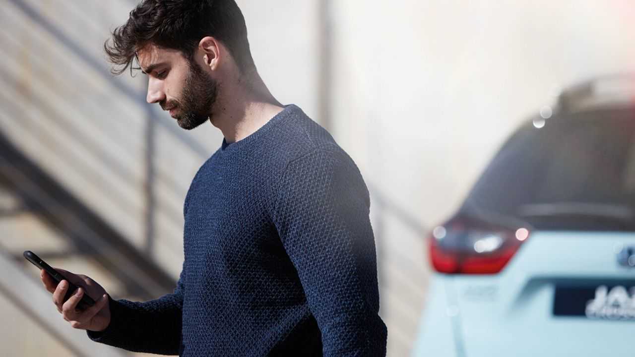 Man looking at My Honda Plus App with Honda Jazz Hybrid Crosstar behind.