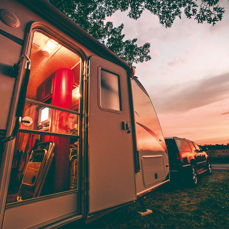 black car with loaded caravan on a campsite during sunset