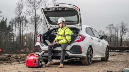 portable power generator standing on the road next to a man in safety jacket sitting in the car boot