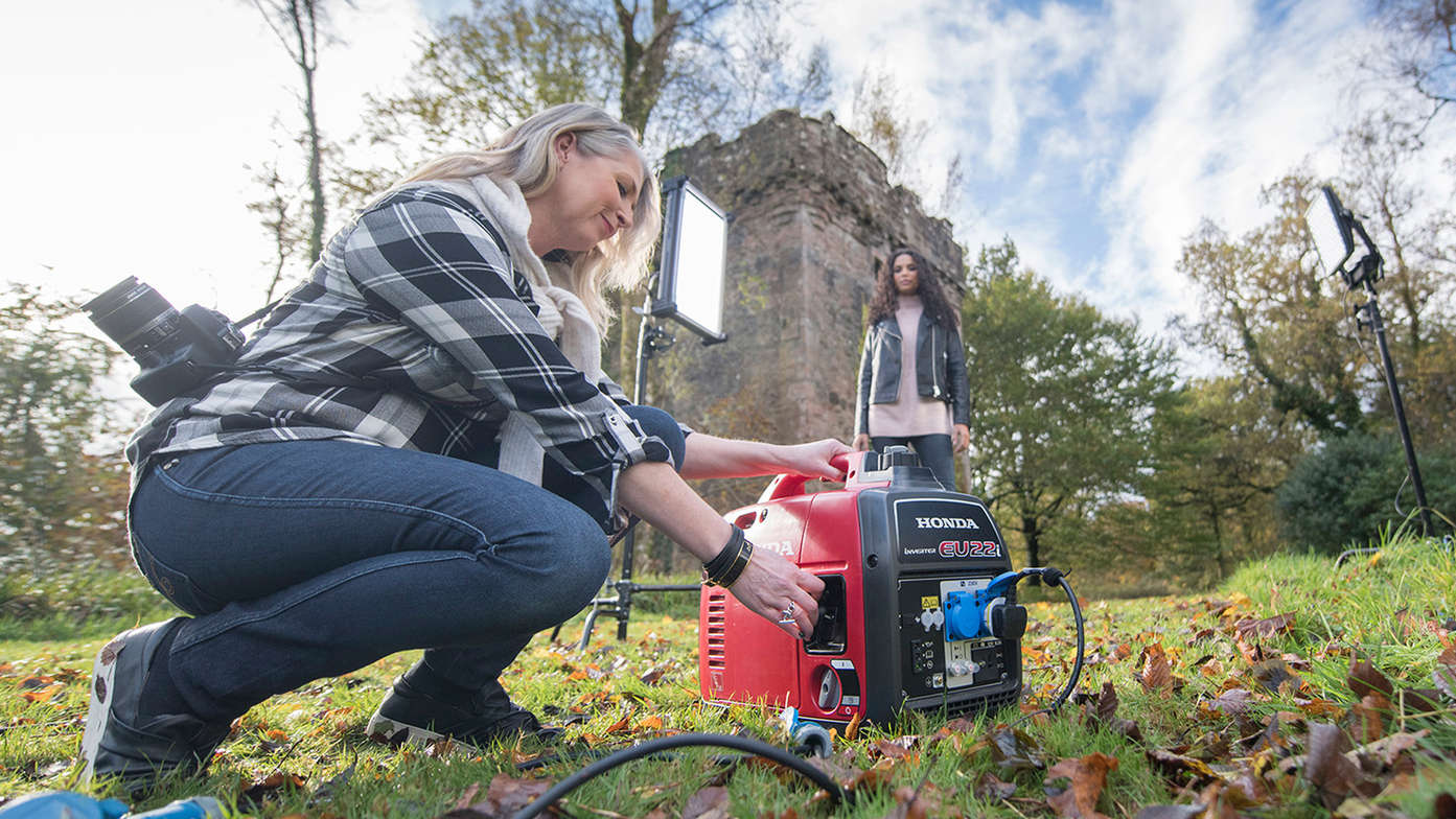 a woman in dark jeans and plaid shirt with camera starting eu22i portable inverter power generator.