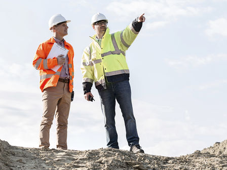 two workers in safety jackets and helmets on a construction site talking