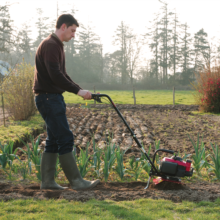 Man pushing Tiller through soil