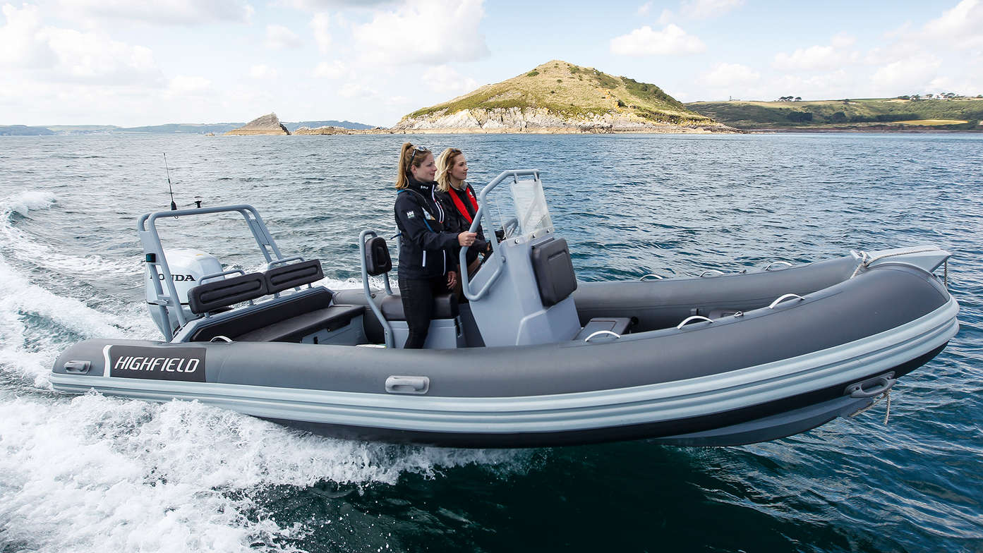 side view of highfield boat with honda outboard engine on water, women standing up driving the RIB