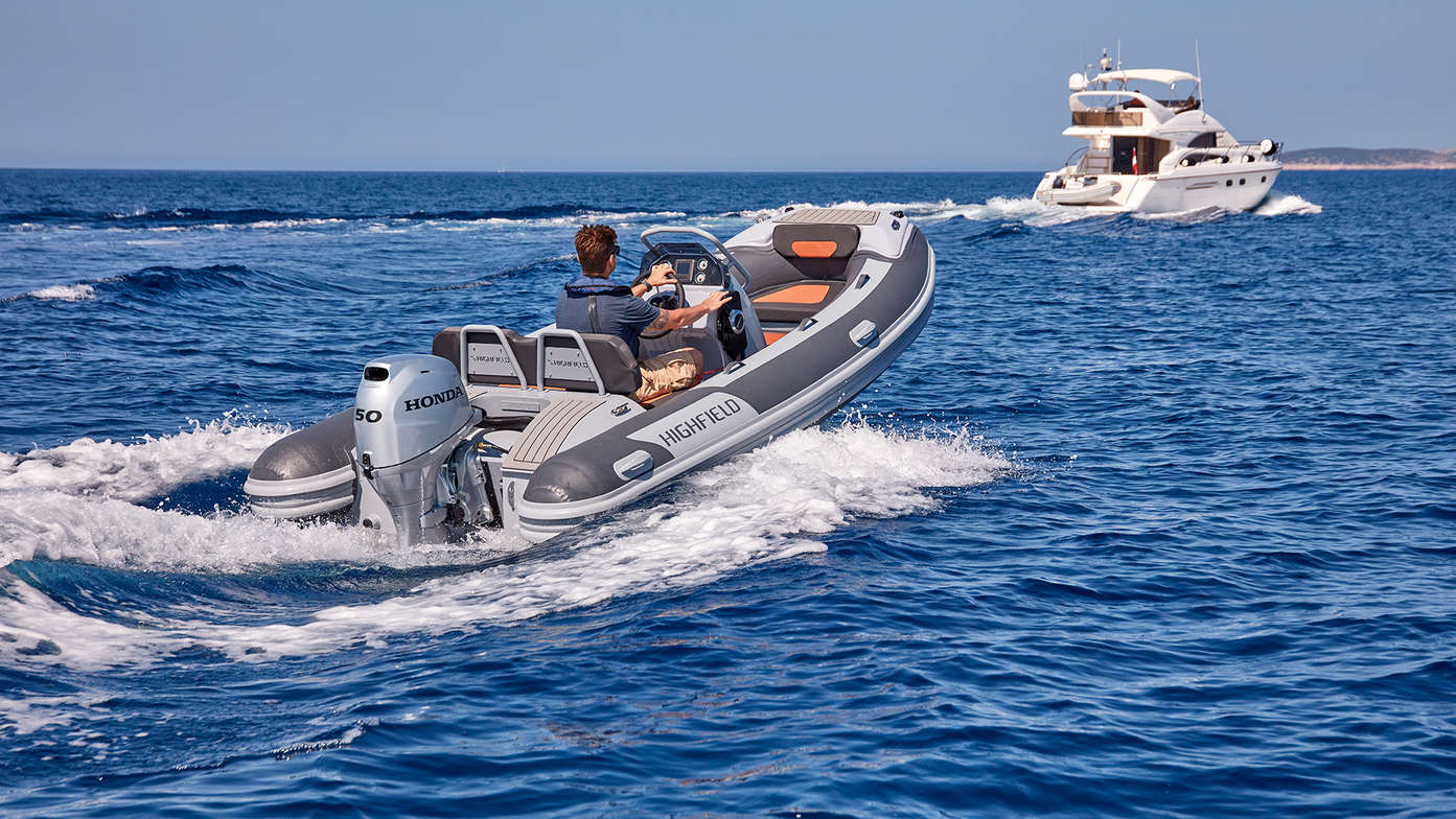 rear angled view of man steering Highfield sport RIB with honda outboard engine on the water