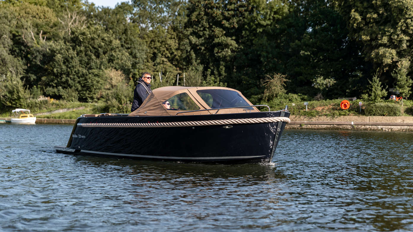 side view of man steering maxima sloop boat on the water