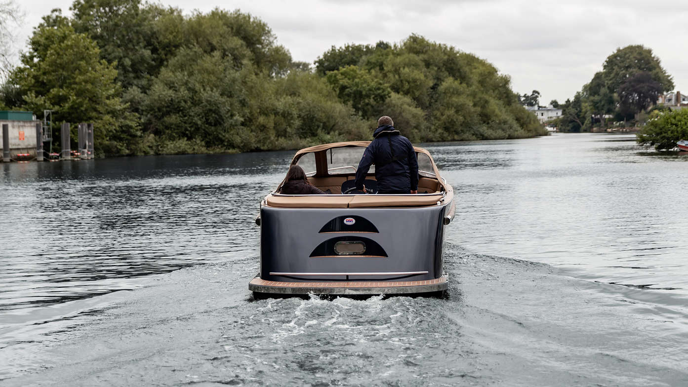 view from behind of man steering maxima sloop boat on the water