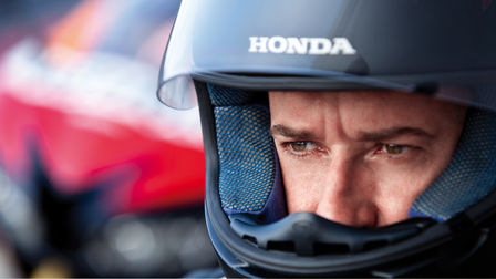 Rider adjusting his right glove sitting. Rear of motorcycle to rider's right.