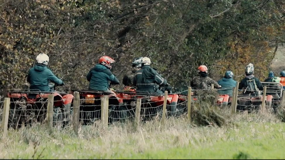 Farmers riding Honda ATVs in a line